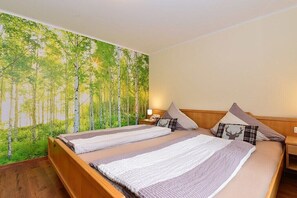 A double bed with a headboard, a nightstand, and a wall mural of a forest. - Eberle Country House (Hirschegg\/Kleinwalsertal)