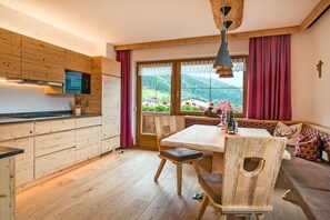A wooden interior with a kitchen, dining table, and a view of a mountainous landscape. - Ziller in the House Fernblick (Mayrhofen)