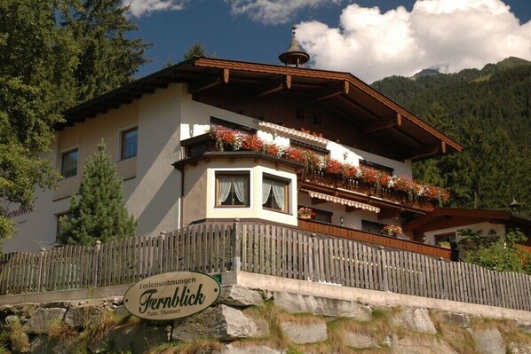 A traditional chalet with a balcony adorned with flowers, a wooden fence, and a sign indicating it's a family-owned lodging. - Ziller in the House Fernblick (Mayrhofen)
