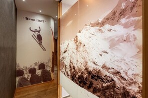Ein Korridor mit einer Wand, die einen Skisprung zeigt und einem großen Poster eines verschneiten Berges.