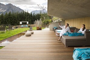 Ein moderner Außenbereich zum Entspannen mit Holzterrasse, Sitzmöbeln und Blick auf die Berge.