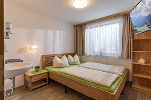 Ein Schlafzimmer mit Bett, Nachttisch, Lampe und einem Fenster mit Vorhängen.