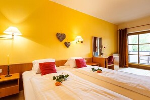 A hotel room with two beds, a desk, a chair, a window with curtains, and a wall with two heart-shaped decorations. - at the country house Luka (Mörbisch)