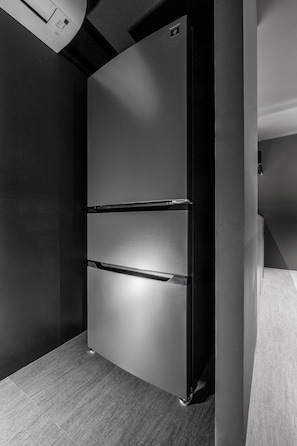 A modern, dark-colored refrigerator with a sleek design, located in a corner of a room with a textured floor. - THE DWBL HOTEL B (Otaru)