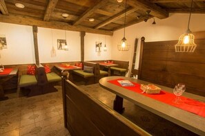 Ein Restaurantinneres mit Holzbalken, Sitzeinheiten und hängenden Lampen.
