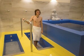 Ein Mann in einem Handtuch steht in einem blauen und gelben Badezimmer mit einer Badewanne und einer Statue.