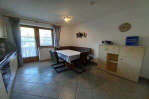Eine kleine Küche mit Esstisch, Stühlen, einem Schrank und einer Wanduhr.