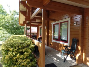 A wooden cabin with a covered porch, a small garden, and a number '25' on the wall.