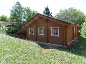 Une maison en bois avec un toit en pente, trois fenêtres et un jardin avec de la pelouse et des fleurs.