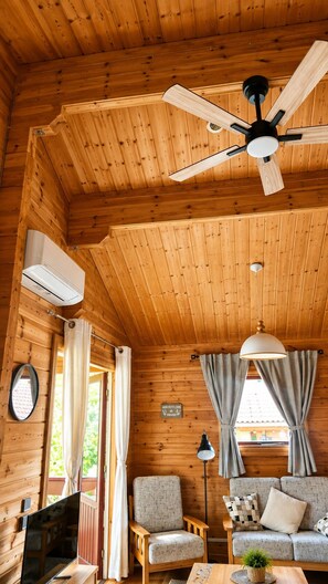 L’intérieur d’un chalet accueillant, avec un ventilateur de plafond, des murs en bois, un canapé, des fauteuils et un téléviseur.