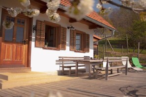 Eine Holzterrasse mit Tisch und Bänken, ein weißes Gebäude mit Holzhörnern und ein grüner Stuhl.