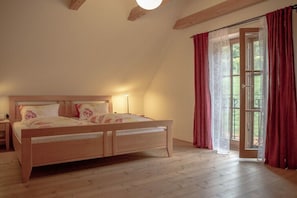 Ein Schlafzimmer mit einem hölzernen Bett, einem Nachttisch, einem Fenster mit Vorhängen und Blick ins Grüne.