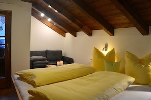 Ein Schlafzimmer mit Holzboden, einem Bett mit gelber Bettwäsche, einem grauen Sofa und einer Wandleuchte.