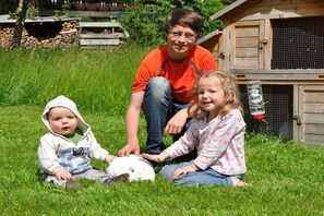 Eine Familie mit einem Kaninchen in einer grünen Parklandschaft, im Hintergrund eine Holzhütte.