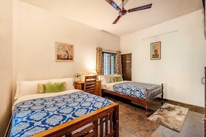 Un dormitorio con dos camas, un ventilador de techo, una ventana con cortinas y una puerta.