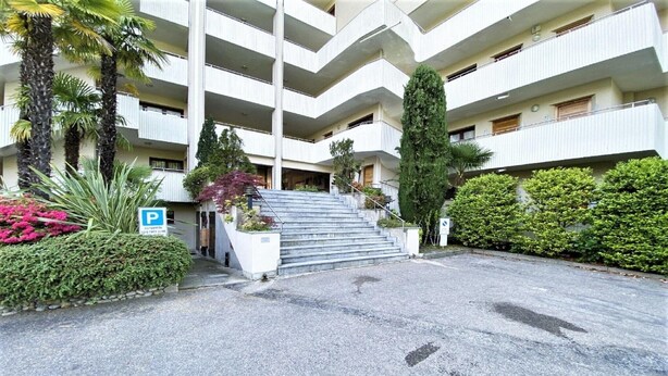 A multi-story building with a parking area, steps leading to the entrance, and surrounding greenery. - Lake View Apartment in Luino for 4 (Luino)