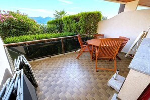 Ein Balkon mit Holztisch und -stühlen, einer Glasbrüstung und Blick auf Grünflächen und Berge.