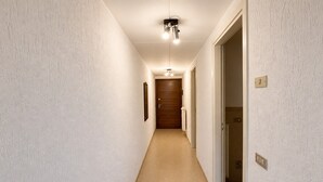 A narrow hallway with a wooden door at the end, a light fixture above, and a wall switch on the right. - Lake View Apartment in Luino for 4 (Luino)