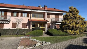 A two-story building with a tiled roof, a balcony on the second floor, and a well-maintained garden with hedges and a tree. - Romantic Lake View Base in Germignaga (Germignaga (VA))
