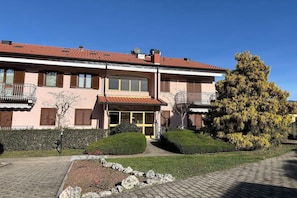 A two-story building with a tiled roof, a balcony on the second floor, and a well-maintained garden with hedges and a tree. - Romantic Lake View Base in Germignaga (Germignaga (VA))