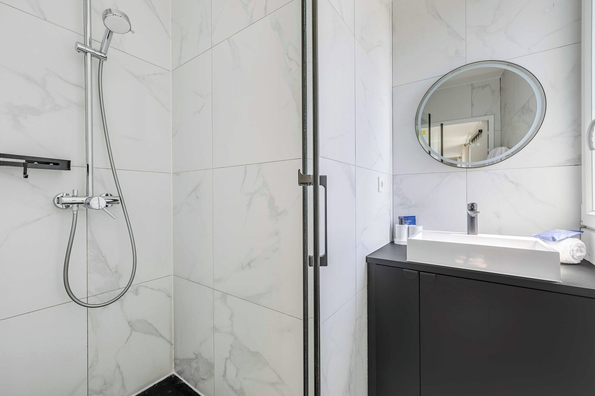 A bathroom with a shower, a sink, a mirror, and a dark cabinet.