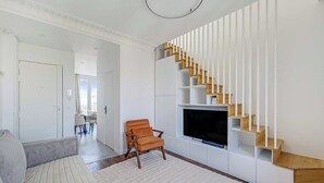 Ett modernt vardagsrum med en soffa, en fåtölj, en tv och en unik trappdesign.