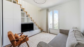 Ett modernt vardagsrum med en trappa, en platt-TV, en soffa och en fåtölj.