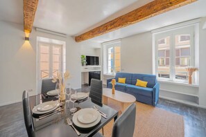 A dining area with a table set for four, a blue sofa, and a television in the background. - 1BDR/4P Apt in the Heart of Saint-Tropez-near Port (Saint-Tropez)