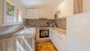 Una cucina moderna con mobili bianchi, forno integrato, microonde e frigorifero.