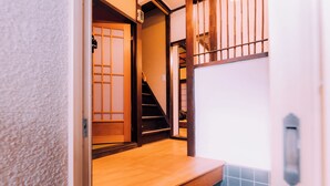 A narrow hallway with a wooden floor, a tiled wall, and a wooden door with a sliding mechanism. - Shinobi House – 4-Bedroom Ninja-Inspired Stay (大阪市)