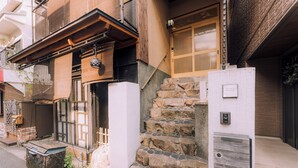 A traditional Japanese building with a wooden staircase, a sliding door, and a small porch area. - Shinobi House – 4-Bedroom Ninja-Inspired Stay (大阪市)