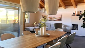 A modern dining area with a wooden table, grey upholstered chairs, a vase with flowers, and pendant lights. - Modern holiday home with sauna (St. Lambrecht)