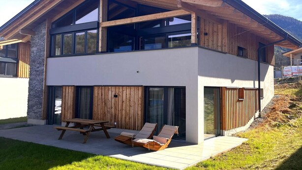 A modern two-story house with a wooden exterior, large windows, and a patio with a table and chairs. - Modern holiday home with sauna (St. Lambrecht)