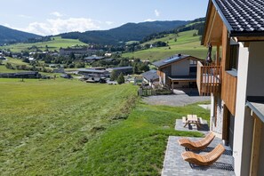 Vue d’un bâtiment doté d’un balcon surplombant un champ verdoyant et un paysage montagneux.