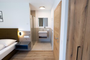 Quarto com cama, mesa de cabeceira e pequena escrivaninha com controle remoto.