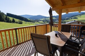 A wooden deck with a table and chairs, overlooking a scenic landscape with hills and a village. - Holiday home on the ski slope with sauna (St. Lambrecht)