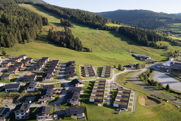 Ein Wohngebiet mit modernen Häusern, die in einem Raster angeordnet sind, umgeben von grünen Feldern und bewaldeten Hügeln.