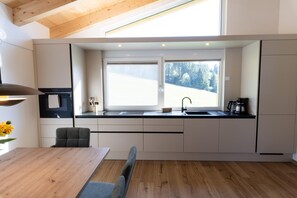 Eine moderne Küche mit einem großen Fenster, einem Essbereich mit einem Holztisch und einem grauen Stuhl.