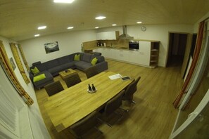 Eine moderne Küche mit weißen Schränken, einem Holzesstisch und einem grauen Sofa mit grünen Kissen.