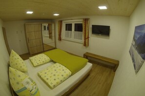 Ein Schlafzimmer mit einem Bett, einem Fenster mit Vorhängen, einem Fernseher, einem Spiegel und einem Bild an der Wand.