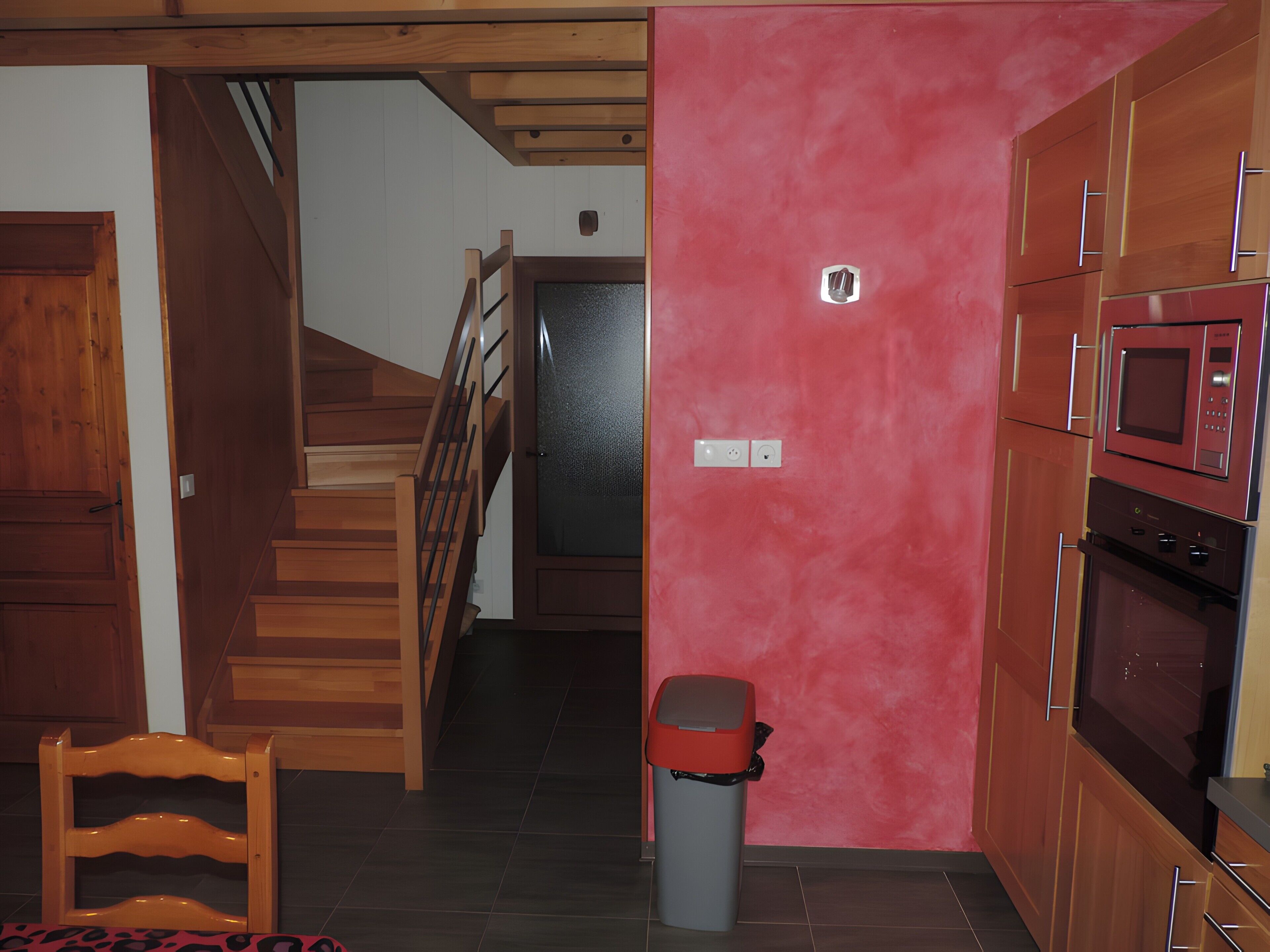 A kitchen with wooden cabinets, a microwave, and a trash bin.