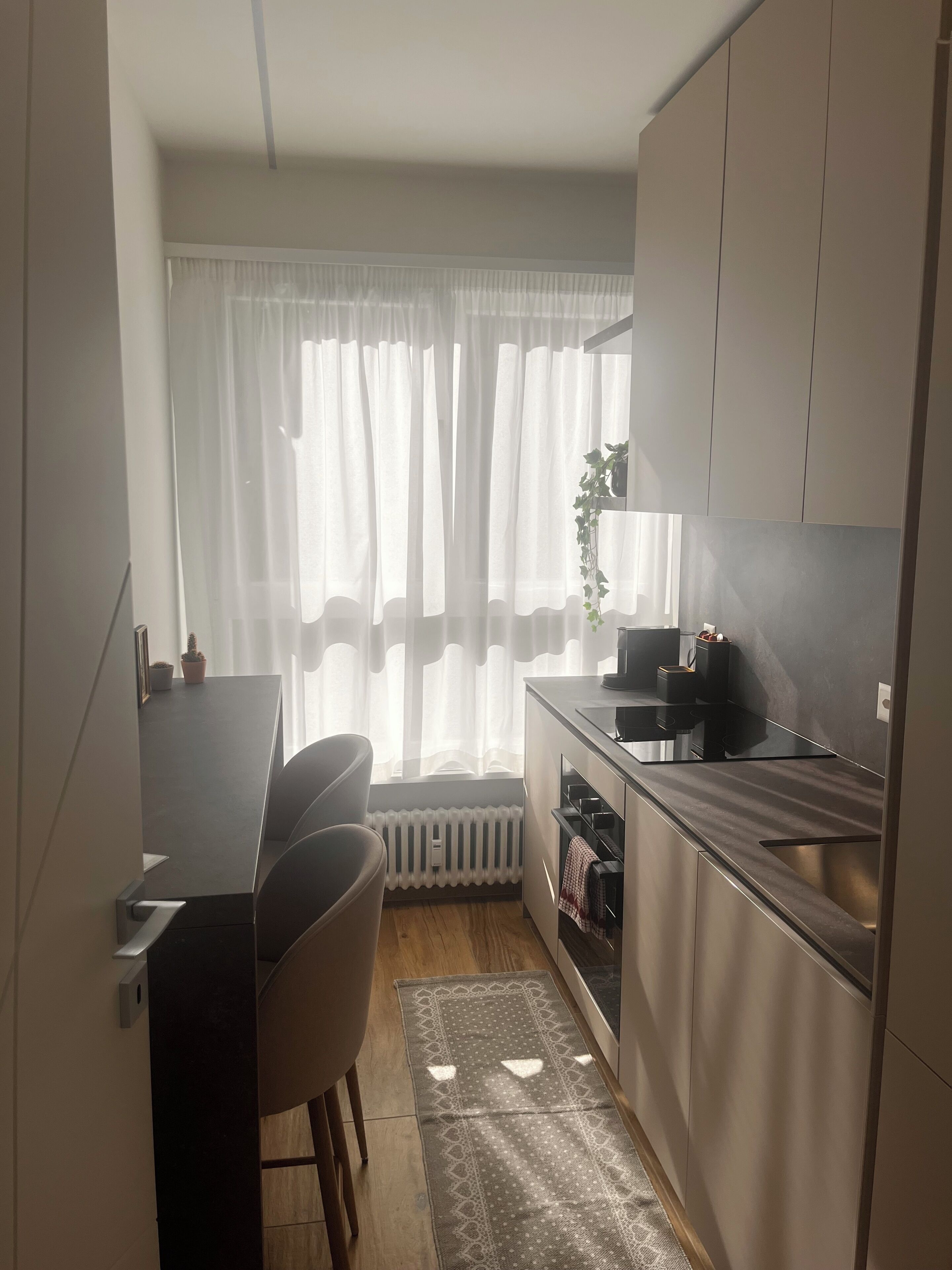 A compact kitchen with a dining area, a radiator, and a window with sheer curtains.