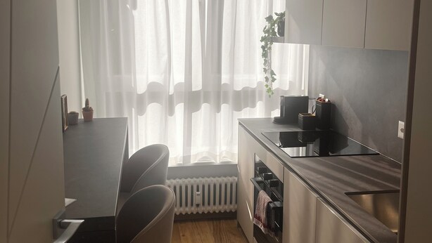 A compact kitchen with a dining area, a radiator, and a window with sheer curtains. - Bright apartment in downtown Lugano (Lugano)