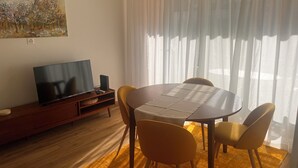 A living room with a flat-screen TV, a painting, a dining table with chairs, and a window with sheer curtains. - Bright apartment in downtown Lugano (Lugano)