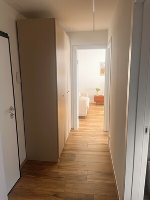 Ein Flur mit Holzboden, weißen Wänden und einem Bett in der Ferne.