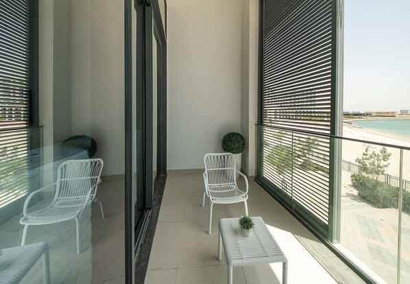 A balcony with two white chairs, a small table with a plant, and a view of a beach.