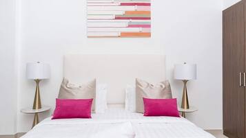 A neatly made bed with white and pink bedding, two bedside lamps, and a wooden wardrobe.