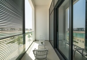 A balcony with a view of a pool and buildings, featuring two white chairs and a small table.