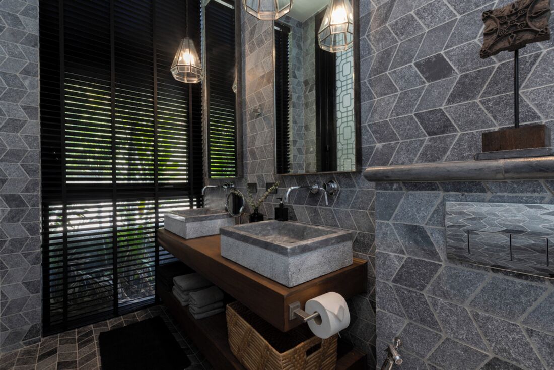 A bathroom with a stone sink, a mirror, and a window with blinds.
