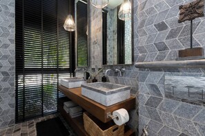 A bathroom with stone walls, a wooden vanity, two sinks, and a large mirror. - Villa Suwan -The Hilltop Escape Samui (Koh Samui)